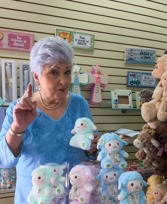 En una tienda Bisel, una señora muestra ovejitas de peluche menta, rosa y celeste frente a cuadros con versículos