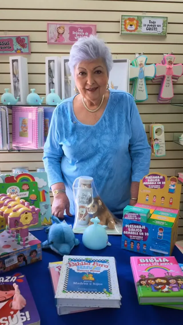 Mesa de una tienda Bisel con Biblias para niños, personajes bíblicos armables y lámparas de ballena, frente a una pared de cuadros con versículos